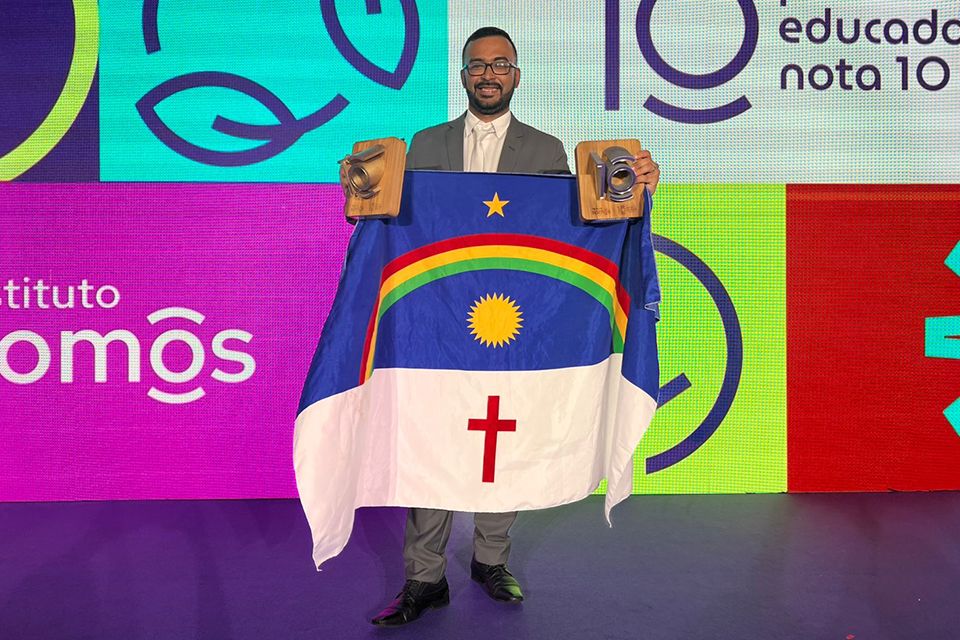 Professor Gustavo Santos Bezerra com os troféus do Prêmio Educador Nota 10 e a bandeira de Pernambuco